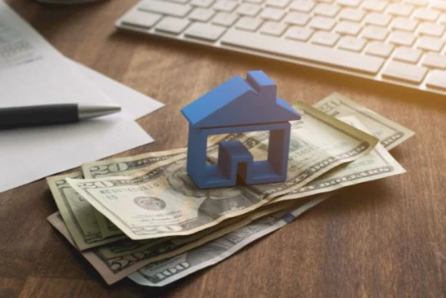 a-blue-home-figurine-resting-on-a-money-with-a-contract-in-the-background a-blue-home-figurine-resting-on-a-money-with-a-contract-in-the-background